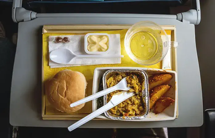 Portion of food for one passenger at airplane board. Indian dish on a folding table on Board the airliner Food served in the plane in economy class. The food in the plane of the top view.; Shutterstock ID 1073480015; Purpose: Plastic free travel tips; Brand (KAYAK, Momondo, Any): momondo