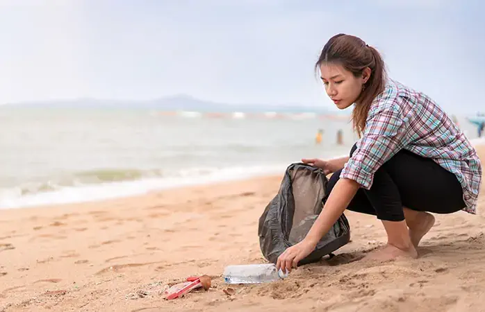 Asian woman picking bottle into plastic bag black for cleaning the beach in morning time, Volunteer concept.; Shutterstock ID 1459499123; Purpose: Plastic free travel tips; Brand (KAYAK, Momondo, Any): momondo