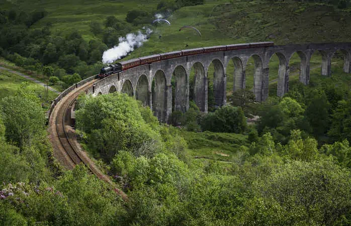 White smoke puffing evocatively from a historic steam train thundering across the iconic arches of the Glenfinnan Viaduct over a green mountain glen deep in the Highlands of Scotland, UK. ProPhoto RGB profile for maximum color fidelity and gamut.